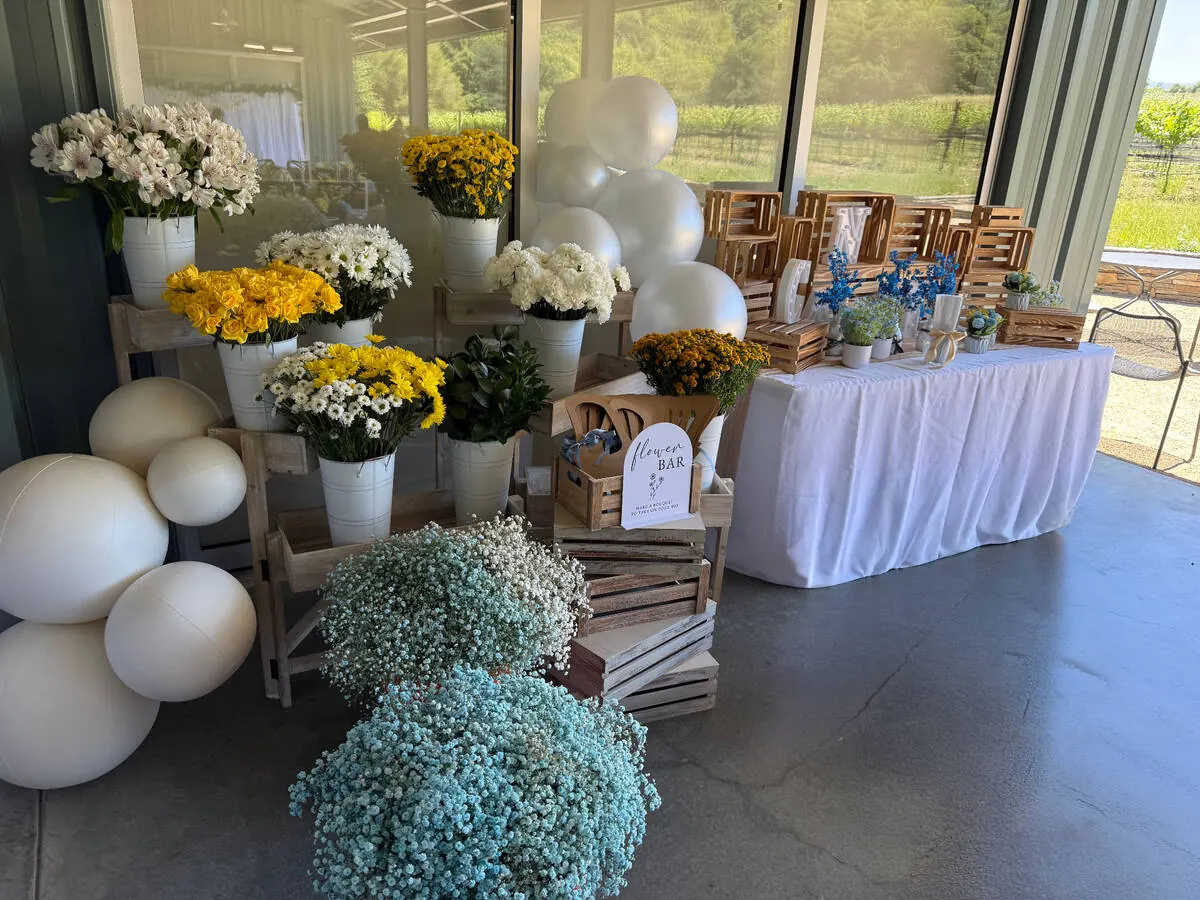 Guest-serve bloom bar of galvanized buckets brimming with butter-yellow roses, daisies and baby's breath with ribbon and wrap laid out — bloom bar add-on from Santa Cruz catering