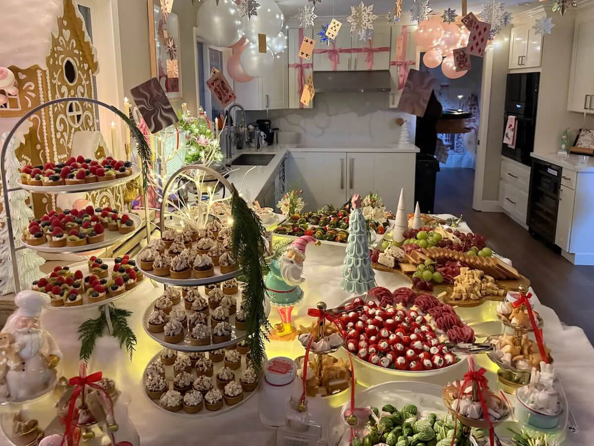 Themed party tablescape where tiered tarts and cupcakes sit beneath pastel balloons with fresh blossoms tucked between the risers — floral party styling for Capitola catering